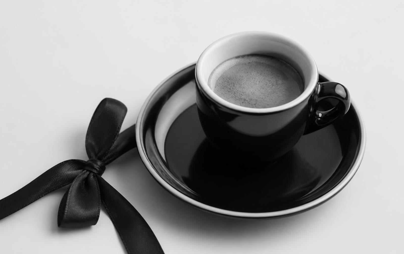 Taza de espresso negra junto a un lazo de regalo, fotografía en blanco y negro